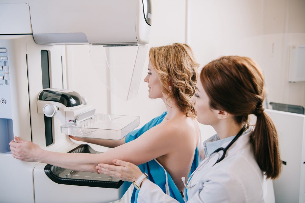 young radiographer standing near patient while making mammography test