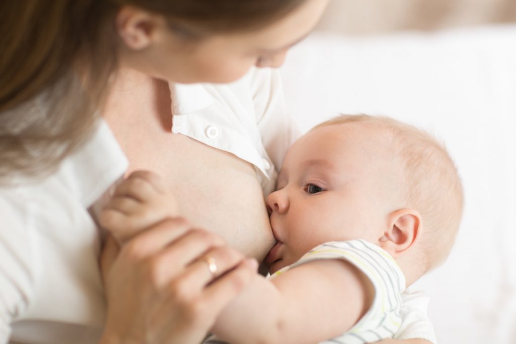 Young mother holding her newborn child. Mom nursing baby. Pretty woman breast feeding kid.