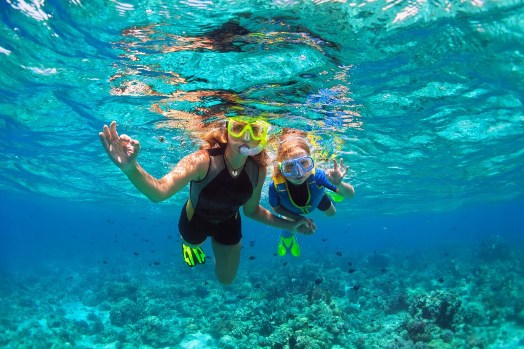 Happy family - mother, kid in snorkeling mask dive underwater with tropical fishes in coral reef sea pool. Show by hands divers sign OK. Travel lifestyle, beach adventure on summer holiday with child.